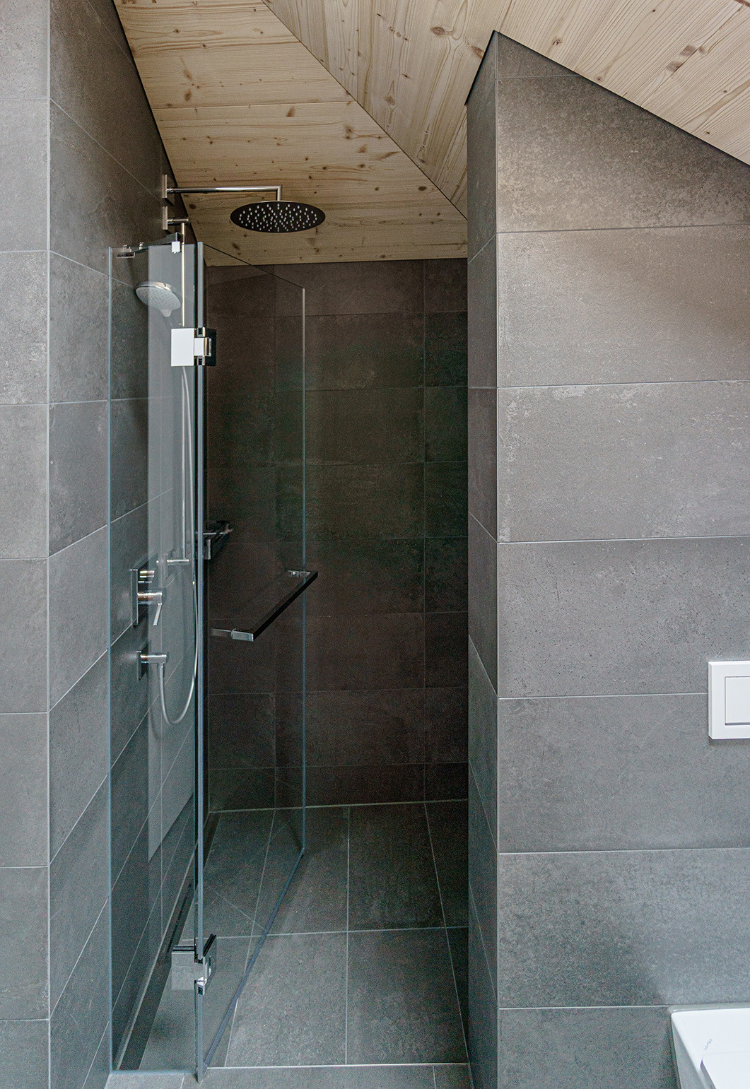 Dusche mit Regenbrause unter Holzschrägdecke, dunkle Steinfliesen